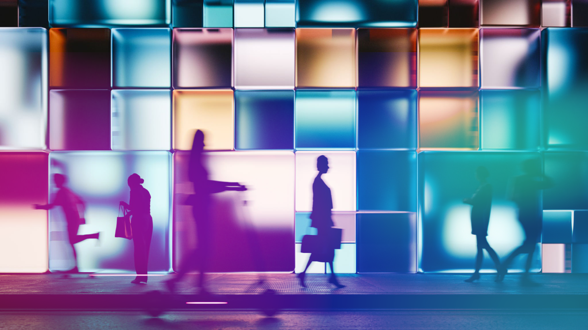 Silhouettes of business people walking past a modern building with colourful illuminated glass panels, captured with motion blur