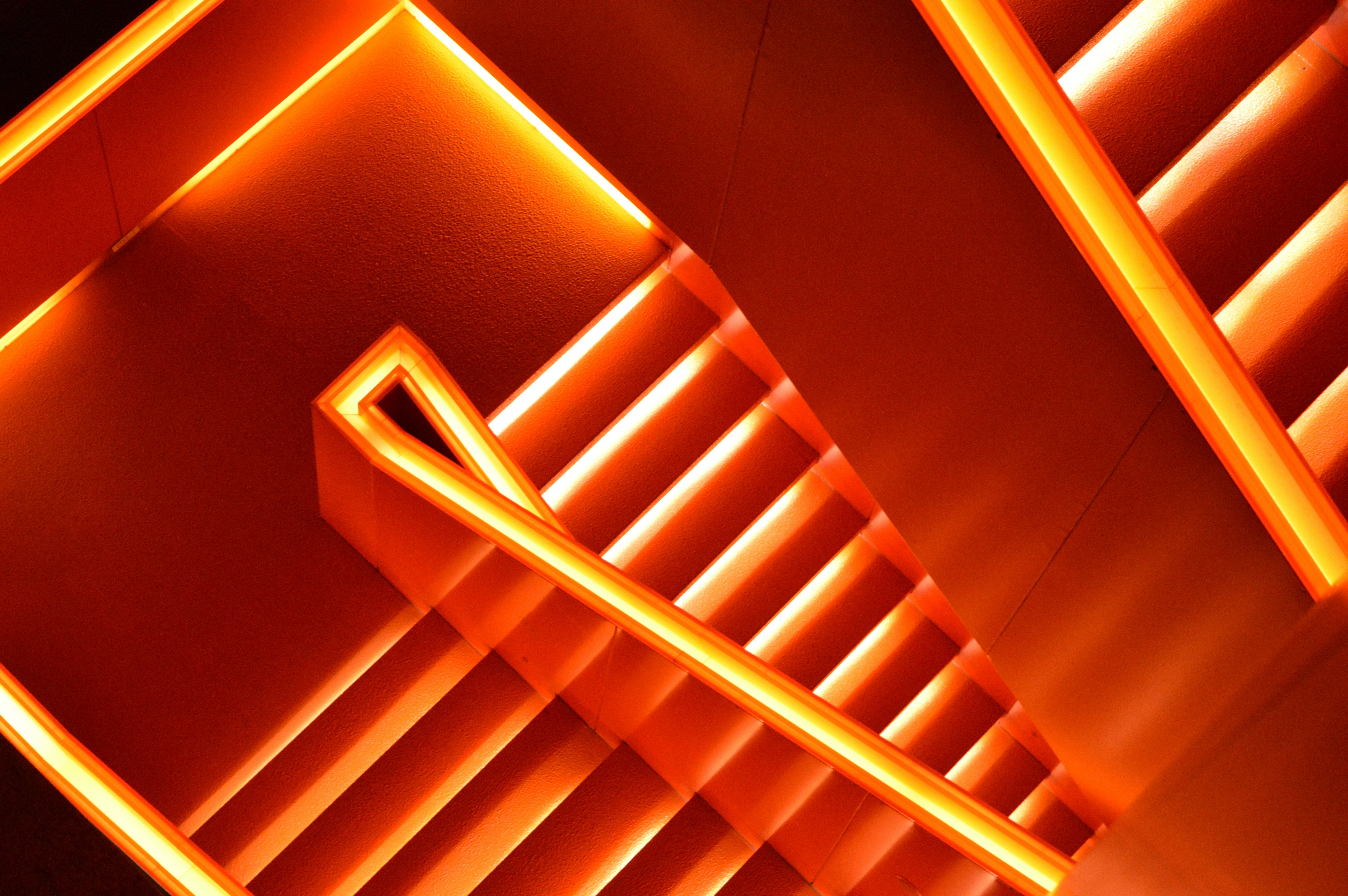 Abstract geometric staircase lit with vivid orange neon lights, viewed from above, creating a bold, modern and futuristic architectural pattern.