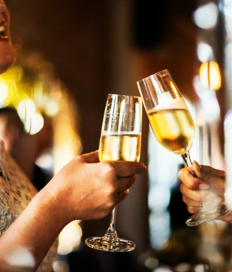 Two people clinking champagne glasses in a warmly lit event setting.